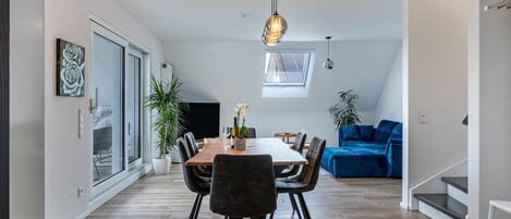 A modern dining area with a wooden table, black chairs, and a hanging light fixture.