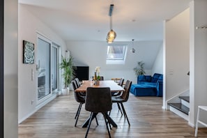 Un espace repas moderne avec une table en bois, des chaises noires et un luminaire suspendu.
