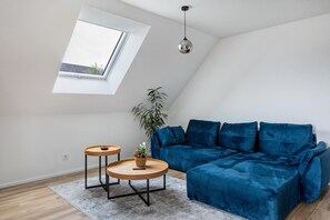 Un salon moderne avec un canapé bleu, deux petites tables rondes en bois, une plante et une lucarne.
