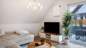 Ein modernes Wohnzimmer mit einer Couch, einem Couchtisch, einem Fernseher, einer Deckenleuchte und einer Topfpflanze.