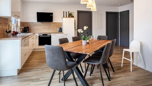 Eine moderne Küche mit einer Holzinsel, einem Essbereich mit Holztisch und -stühlen sowie einem an der Wand befestigten Fernseher.