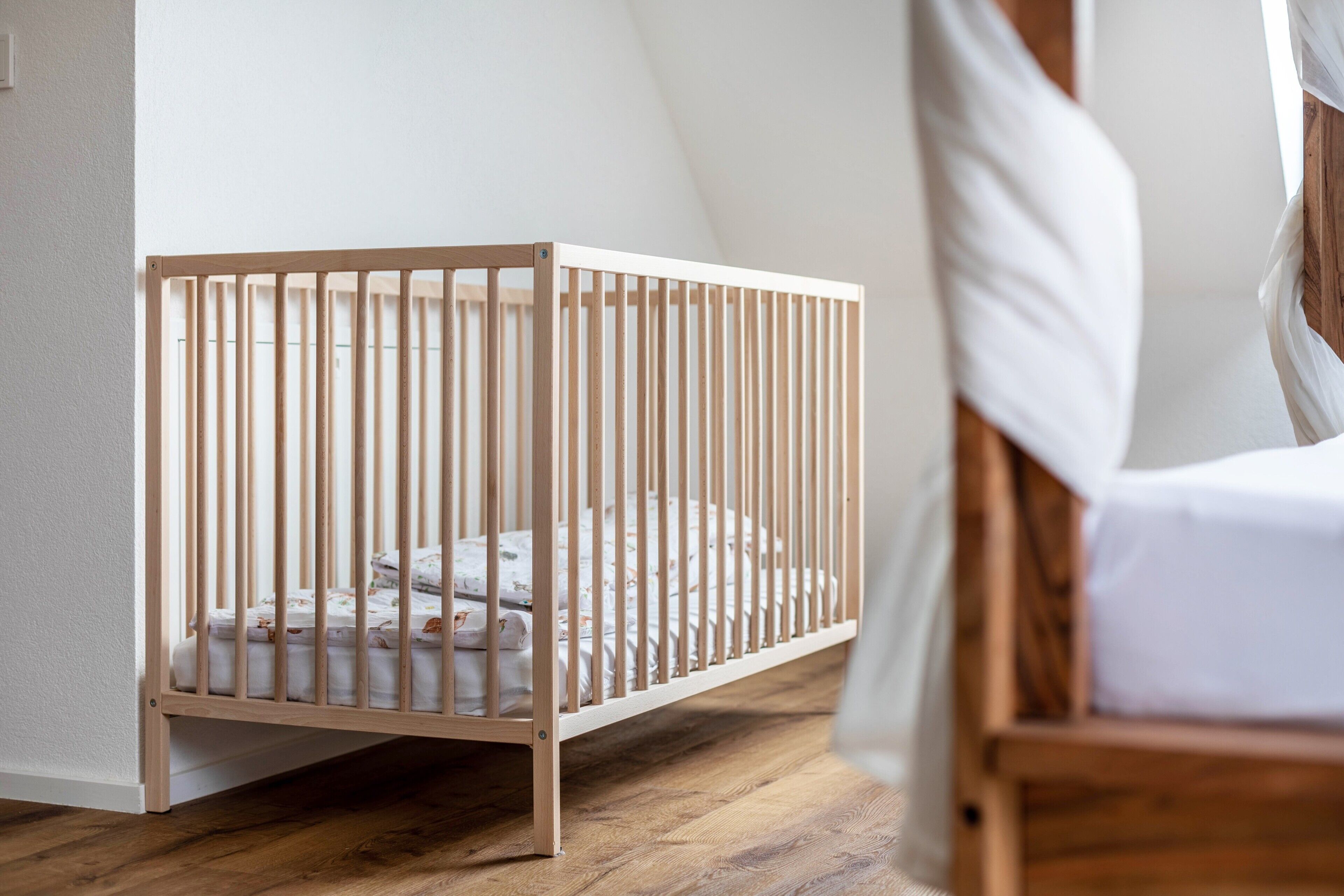 Een houten ledikant met matras en beddengoed, geplaatst tegen een witte muur in een kamer met houten vloer.