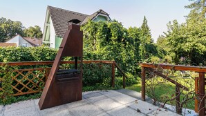 Eine Terrasse mit einem Holzbalkon, einem Metallgrill und Blick auf ein Haus mit einem Ziegeldach.