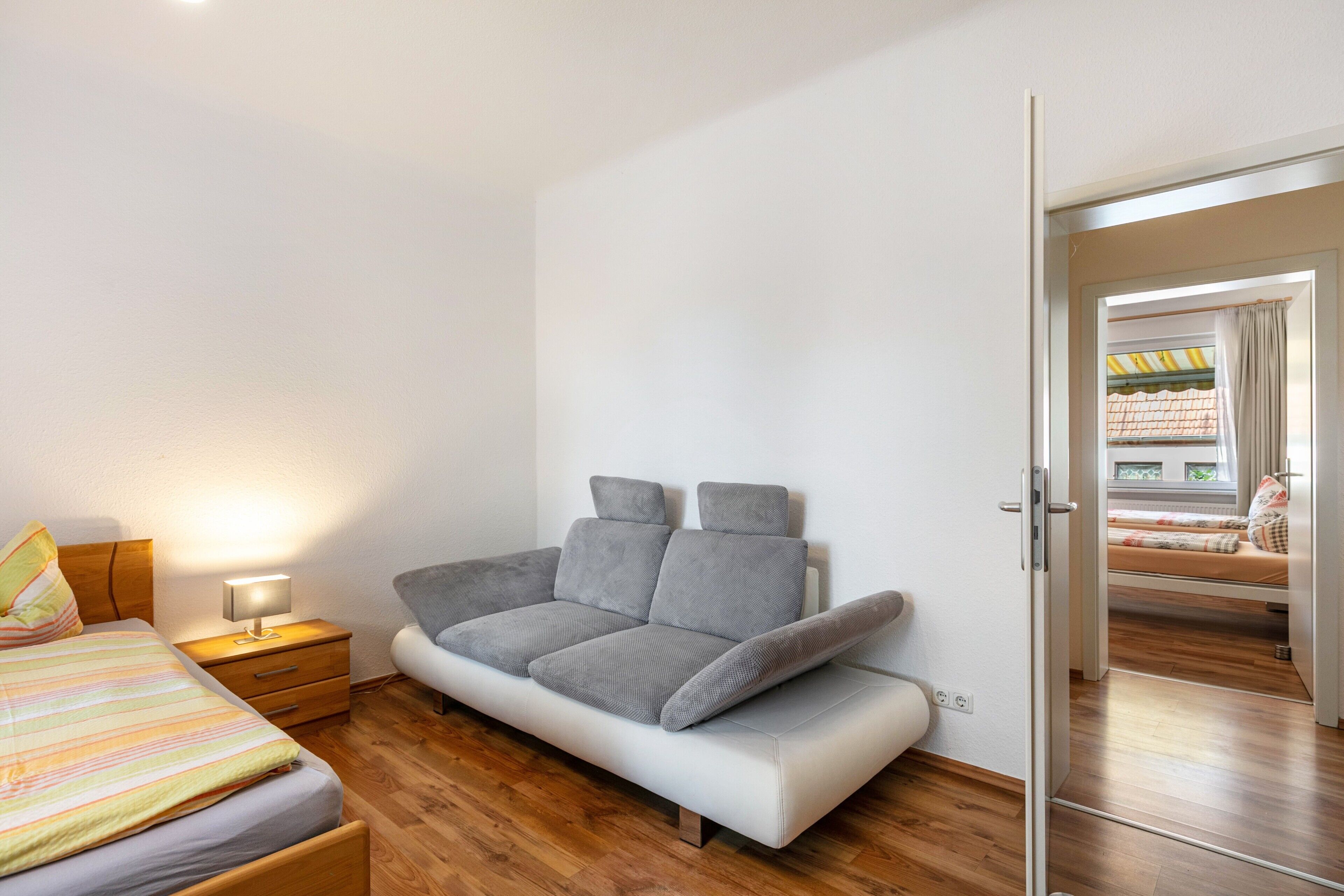 Un dormitorio moderno con sofá cama, una mesita de noche con lámpara y suelo de madera.