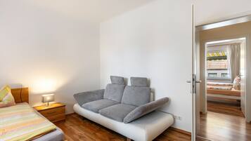 Un dormitorio moderno con sofá cama, una mesita de noche con lámpara y suelo de madera.