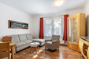 Un salon comprenant un canapé, un fauteuil, une petite table, un meuble en bois et un tableau accroché au mur.