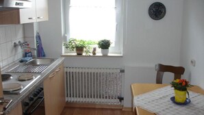 A compact kitchen with a window, a radiator, a stove, and a dining table with a chair. - Apartment 'Waldesruh' with Private Terrace and Wi-Fi (Sölden)