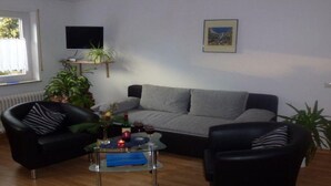 A living room with a grey sofa, two black armchairs, a glass coffee table, a TV on a stand, and a framed picture on the wall. - Apartment 'Waldesruh' with Private Terrace and Wi-Fi (Sölden)
