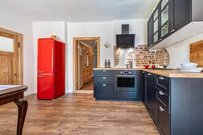 A kitchen with a red refrigerator, wooden cabinets, a brick backsplash, and a wooden door.