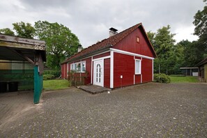 A red barn with a white door and windows, a gravel driveway, and a green structure labeled '26' in the background. - Holiday Home 'Haus Vierjahreszeiten' with Private Garden (Groß Niendorf)