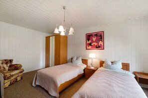 A bedroom with two beds, a wardrobe, a nightstand, a lamp, a chair, and a wall art piece. - Holiday Home 'Haus Vierjahreszeiten' with Private Garden (Groß Niendorf)