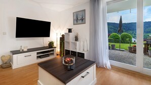 Un soggiorno moderno con una TV a schermo piatto, un tavolino da caffè con oggetti decorativi, una porta scorrevole in vetro che dà su un giardino e un design minimalista.