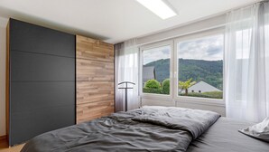 Una camera da letto con un letto, un armadio, una finestra che mostra una casa e alberi, e una lampada a soffitto.