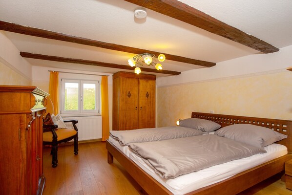 A bedroom with a wooden bed, a wooden wardrobe, and a window with curtains.