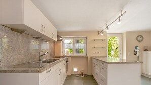 Une cuisine moderne dotée de plans de travail en granit, de meubles blancs, d’un évier encastré et d’une fenêtre donnant sur un espace verdoyant.