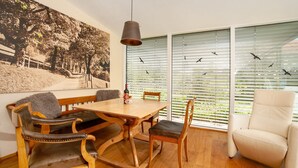 Un coin repas avec une table et des chaises en bois, un grand tableau accroché au mur et une fenêtre avec des stores.