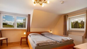 Un lit simple avec un cadre en bois, deux tables de chevet avec des lampes, une chaise et deux fenêtres avec des rideaux.