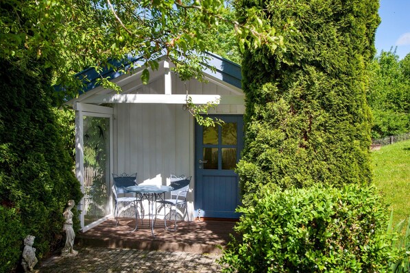 Un espace extérieur abrité, aménagé avec une table et des chaises, et entouré d’une végétation luxuriante.