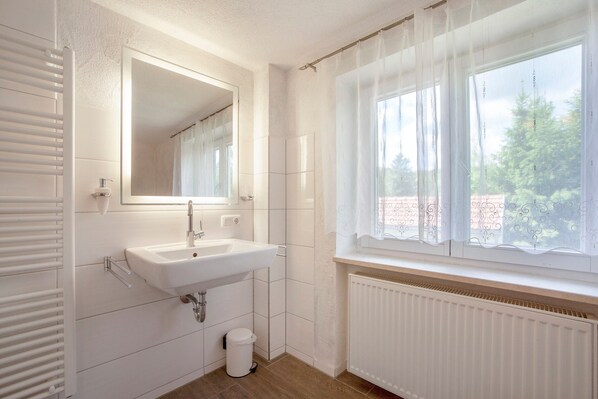 Un baño con un lavabo blanco, espejo y ventana con cortinas.