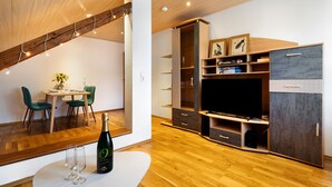 Una sala de estar moderna con techo de madera, comedor con sillas verdes, televisor de pantalla plana y estanterías empotradas.