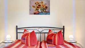Ein Bett mit roten Kissen, ein Sonnenblumenbild und zwei Nachttischlampen.