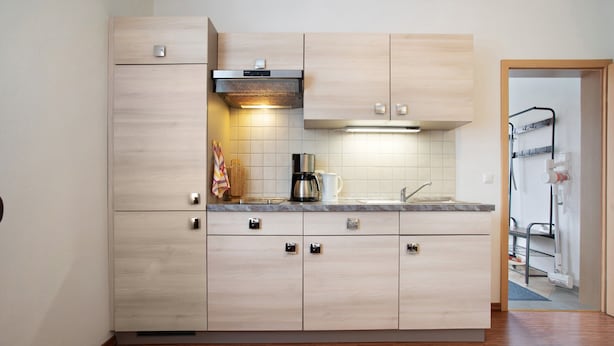 Eine moderne Küche mit hellen Holzschränken, einer Edelstahl-Dunstabzugshaube und einer integrierten Kaffeemaschine.