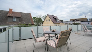 Eine Dachterrasse mit Tisch und Stühlen, einer Brüstung und Blick auf Wohnhäuser.