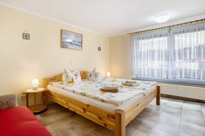A wooden bed with a floral bedspread, a bedside lamp, and a window with sheer curtains.