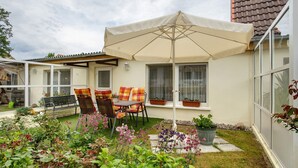Eine Terrasse mit Tisch, Stühlen, einem großen Sonnenschirm und Topfpflanzen.