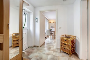 A hallway with a wooden door, wicker baskets, a dining area with a table and chairs, and a kitchen area with a microwave.
