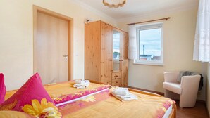 Un dormitorio con cama, armario, silla y ventana.