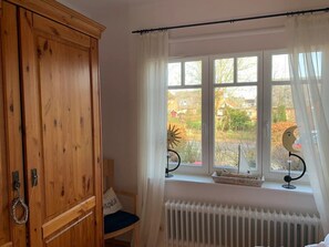 Una habitación con armario de madera, un radiador, una ventana con cortinas y una silla con cojín.