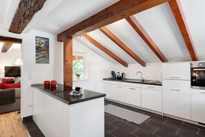 A modern kitchen with white cabinets, a black countertop, and exposed wooden beams. - Apartment 'Vogtshaus De Luxe' with Mountain View, Private Terrace for 13 Guests (Gernsbach)