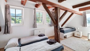 Een slaapkamer met twee bedden, houten balken, uitzicht op groen en een witte radiator.