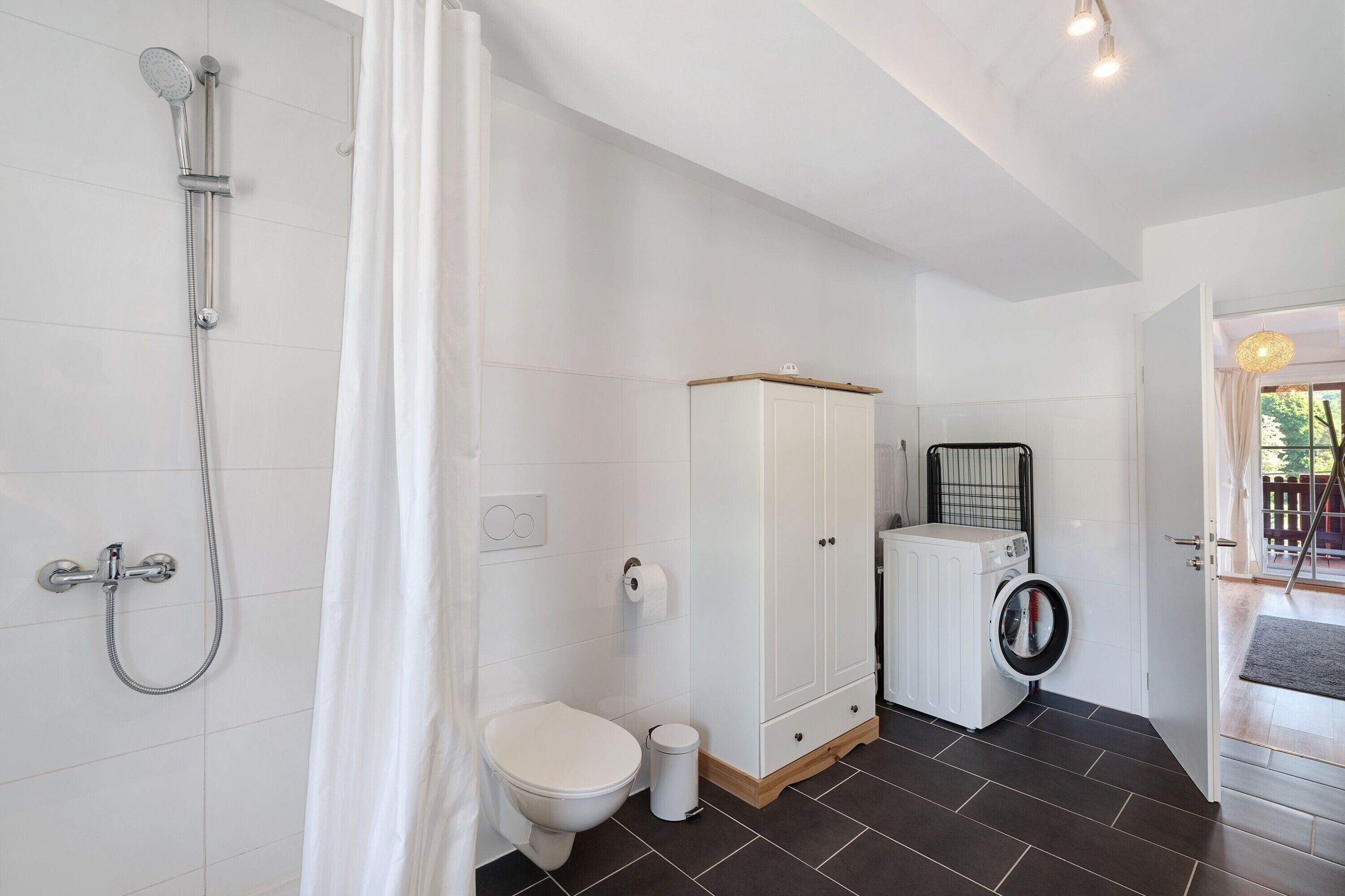 Een badkamer met douche, toilet, kast en wasmachine.