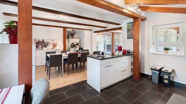 Een moderne keuken met witte kasten, een houten plafond en een eethoek met stoelen en een tafel.