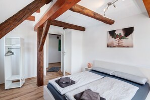 A bedroom with a bed, wooden beams, a white wardrobe, and a door leading to another room. - Apartment 'Vogtshaus De Luxe' with Mountain View, Private Terrace for 13 Guests (Gernsbach)