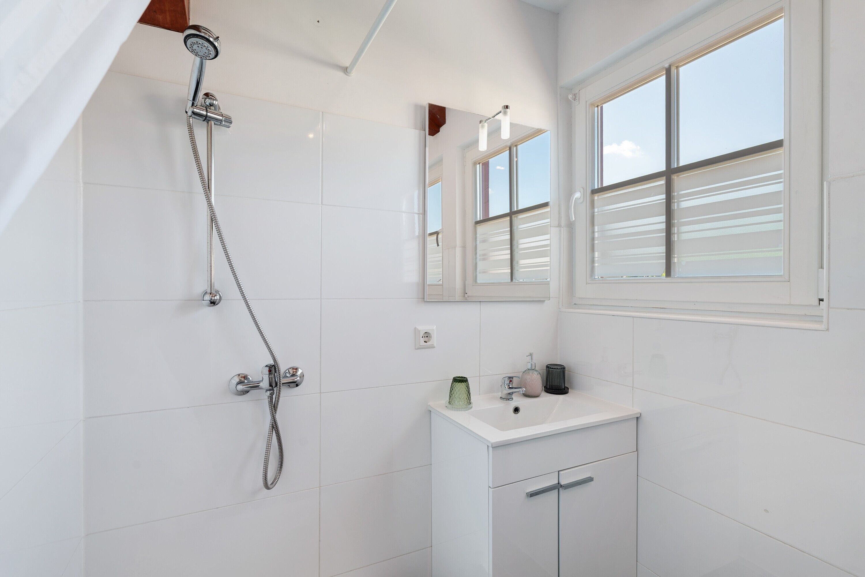 Ein Badezimmer mit Dusche, Waschbecken, Spiegel und Fenster.