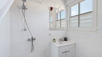Ein Badezimmer mit Dusche, Waschbecken, Spiegel und Fenster.