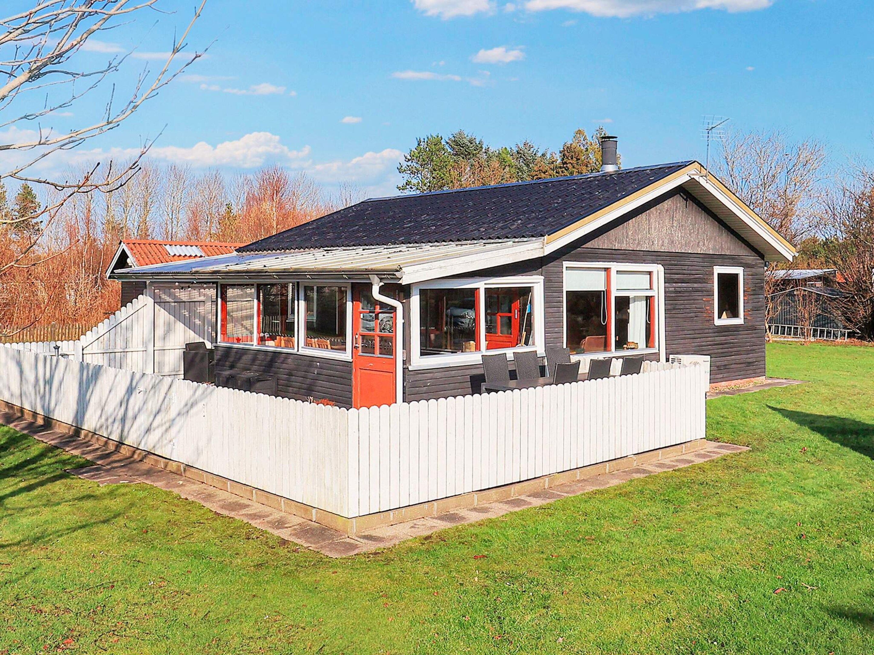 A single-story house with a covered porch, a fenced yard, and a clear sky.