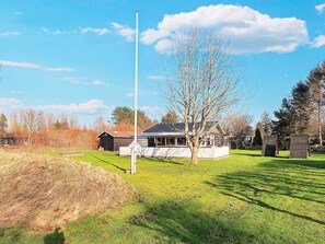 A grassy area with a flagpole, a tree, and a building with a sloped roof. - 5 Person Holiday Home in Hals (Hals)