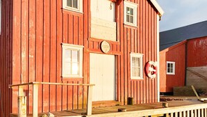 Un edificio de madera roja con puerta y ventanas blancas, y un pequeño porche con barandilla.