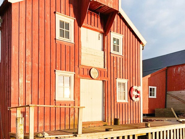 Ein rotes Holzgebäude mit weißer Tür, Fenstern und einer kleinen Veranda mit Geländer.