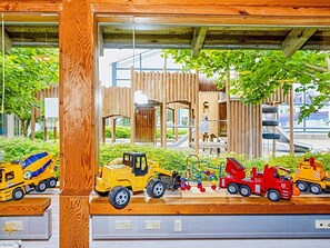 Children can play and explore in this enclosed play area featuring a slide, climbing structures, and toy vehicles.