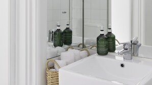 Ein Badezimmer mit einem großen Spiegel, weißen Fliesen, einem weißen Waschbecken und zwei Olivenölflaschen.