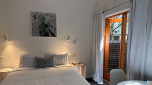 Ein Hotelzimmer mit Bett, Nachttischen, Schreibtisch und Stuhl. Ein Fenster mit Vorhängen bietet einen Blick nach außen.