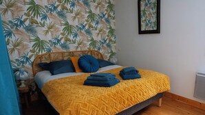 Een bed met een geel gebreid dekbed, blauwe kussens en opgevouwen handdoeken.