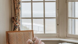A room with a large window overlooking a beach, a chair with a patterned cushion, and a vase with flowers. - Beautiful Normandy Villa in an Exclusive Location (De Haan)