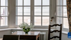 A room with a bay window overlooking a beach, a wooden table with a green glass bowl, and a chair. - Beautiful Normandy Villa in an Exclusive Location (De Haan)