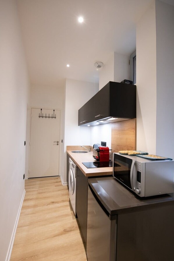 A compact kitchen with a washing machine, a microwave, and a coffee maker. - Opera 7 – Studio downtown – Place des Terreaux (Lyon)